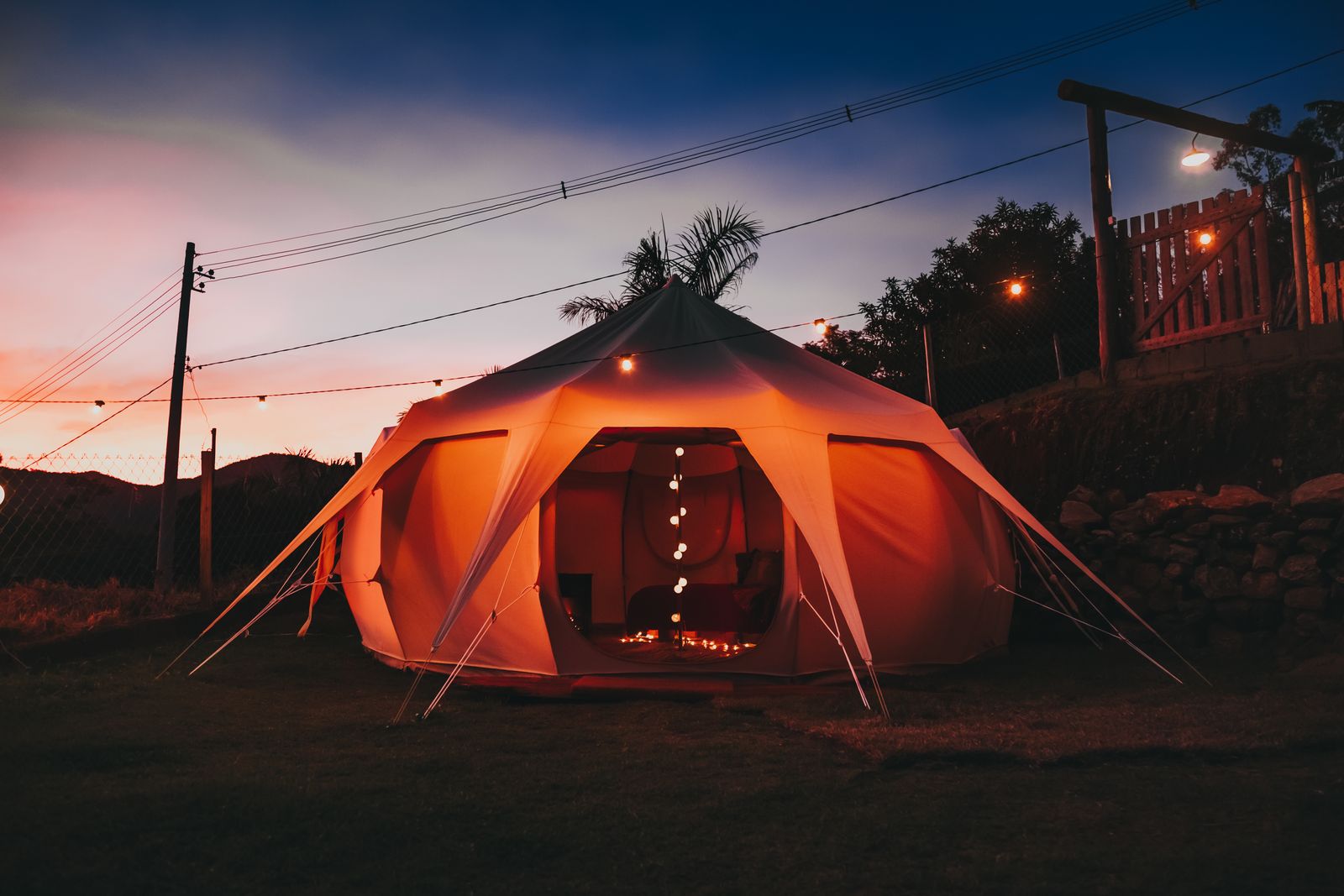 A glamping bell tent glowing with string lights against a twilight sky